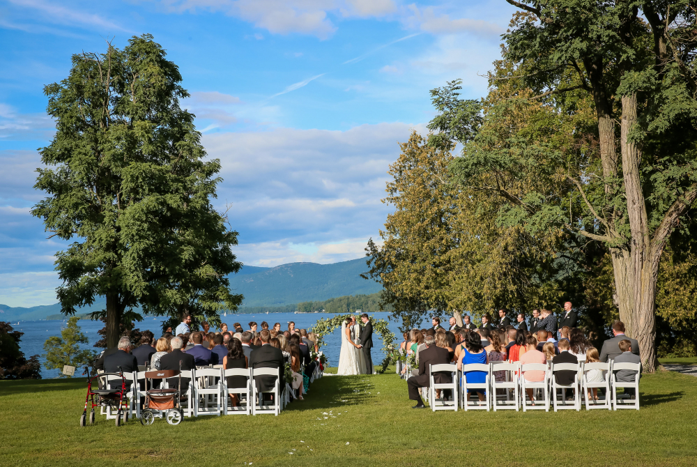 Wedding ceremony with white chairs and floral arch overlooking Lake George with the Adirondack mountains in the background
