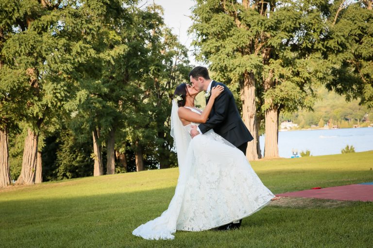 Bride and groom embrace on lawn in front of lake
