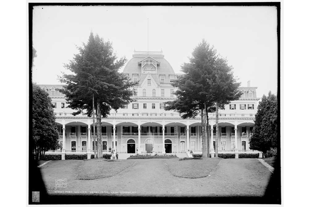 Tall pines frame the Fort William Henry Hotel Entrance