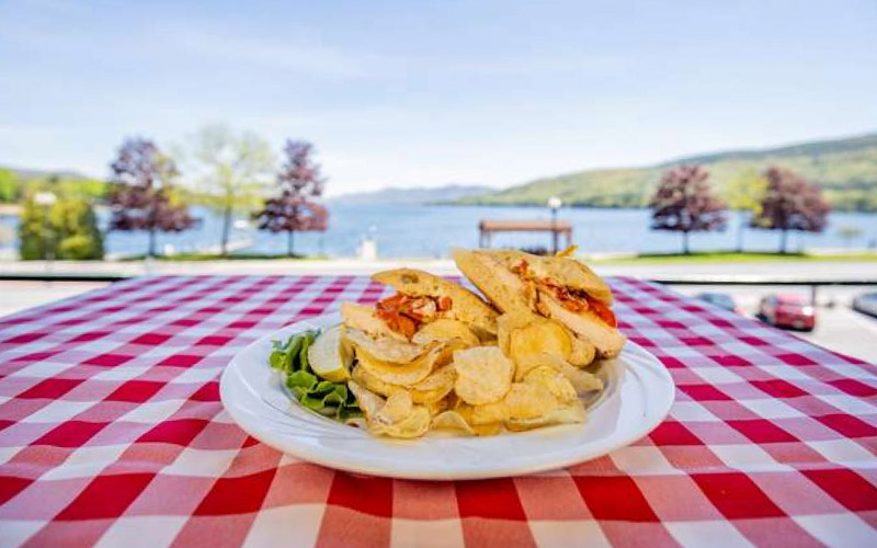 sandwich and chips on a plate in front of lake george
