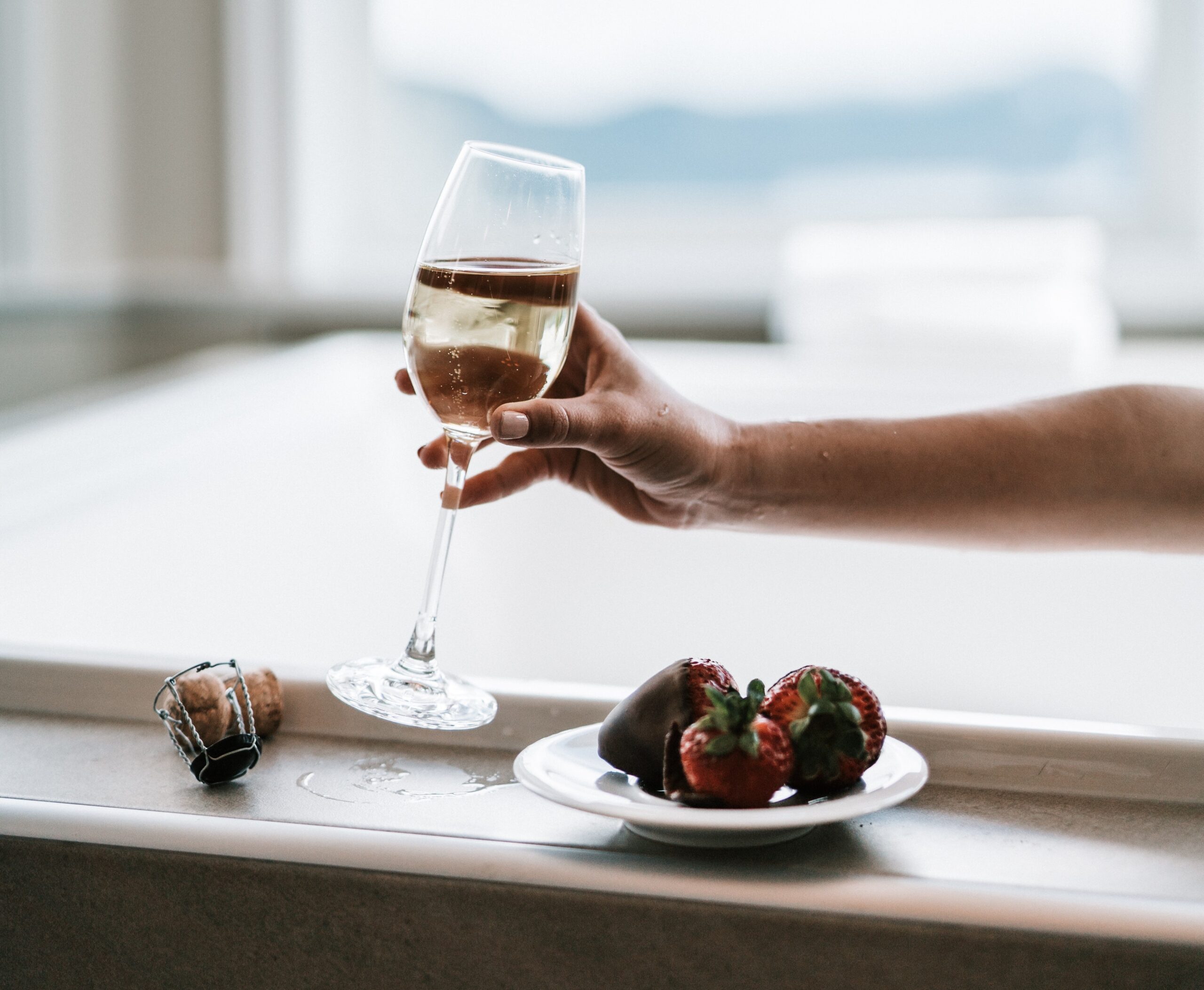Hand holding wine glass with strawberries on plate