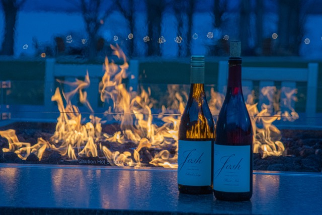 Two bottles of wine next to a fire table at dusk